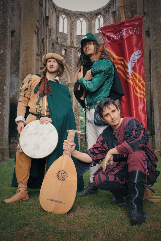 Les trois musiciens du groupe de bardcore Courseval posent dans l'église abbatiale de Hambye avec leurs instruments et leur étendard.