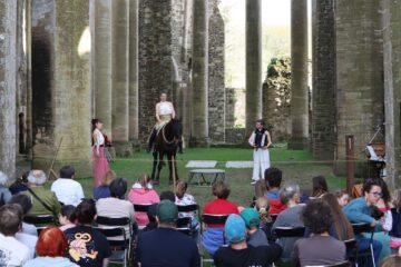 Spectacle dans l'église abbatiale. On voit le public au premier plan, deux chanteuses entourant un cheval et sa cavalière.