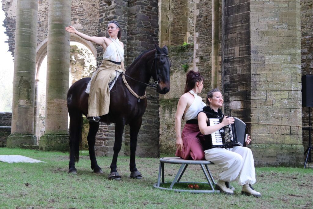 Concert équestre dans l'église abbatiale. deux chanteuse sont assises sur un tabouret, une autre est assise sur son cheval noir derrières elles.