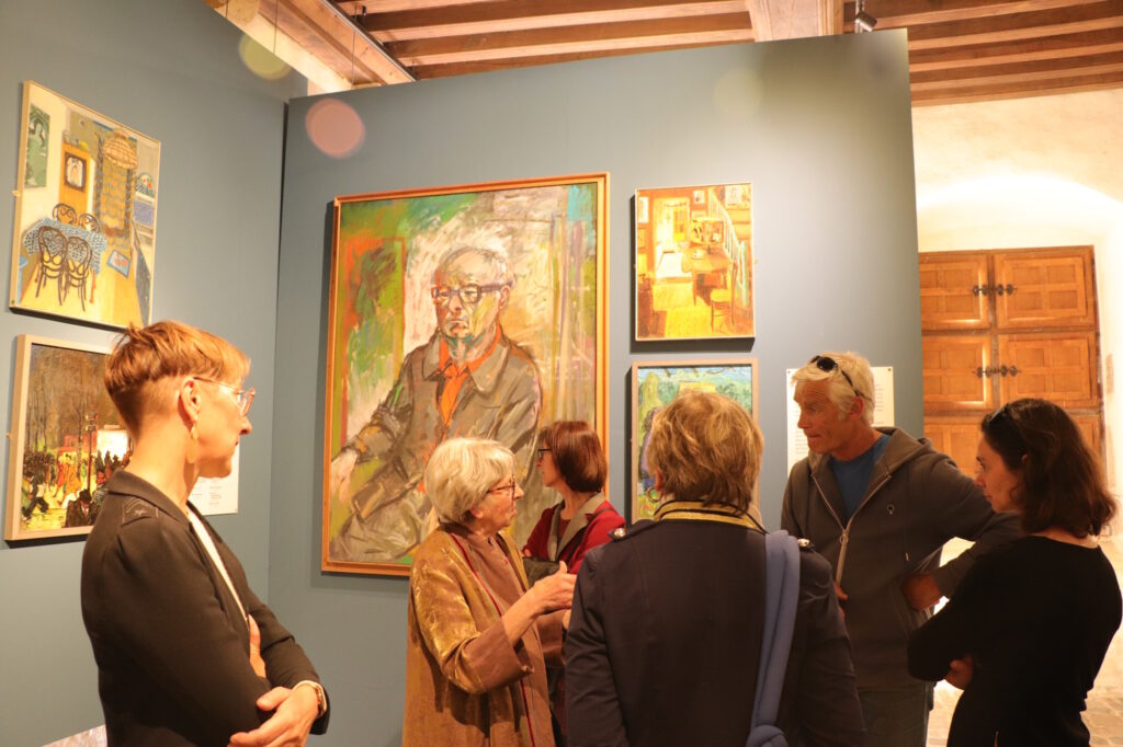 Quelques invités de l'inauguration de l'exposition Les Paysages de Robert Surcouf. Maud Beck, la fille de l'artiste, explique la vie de son père devant un grand portrait de lui par Jacques Pasquier.