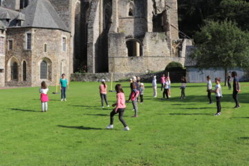 Un groupe scolaire pratique un atelier chorégraphique devant le chevet de l'église abbatiale de l'abbaye de Hambye