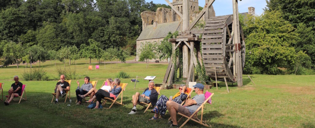 Les participants du festival Les rayonnantes prennent le soleil devant la grange de l'abbaye. En fond on aperçoit la grue et l'église abbatiale.