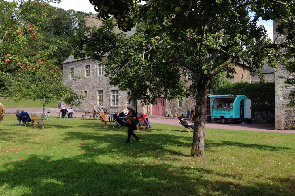 La caravane du food truck Au Cornet de crêpes est installée devant le logs abbatiale et les visiteurs sont installés autour pour manger.