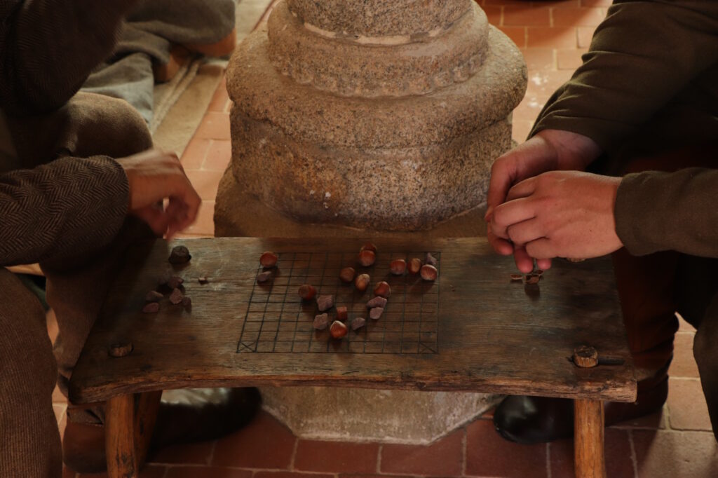 L'image montre un plateau de jeu médiévaux. Le sjetons sont des graviers et des noisettes.
