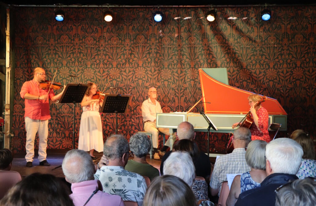 Concert sous la grange. 4 musiciens se tiennent sous la scène.