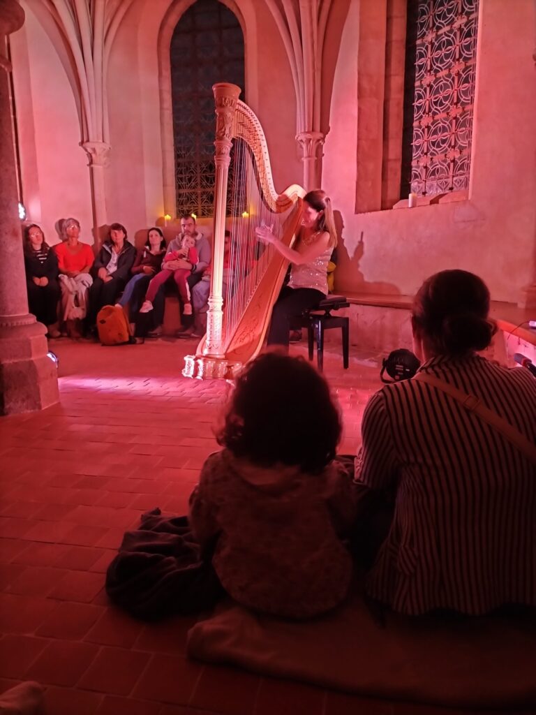 Une harpiste joue dans la salle capitulaire, dans une lumière rose