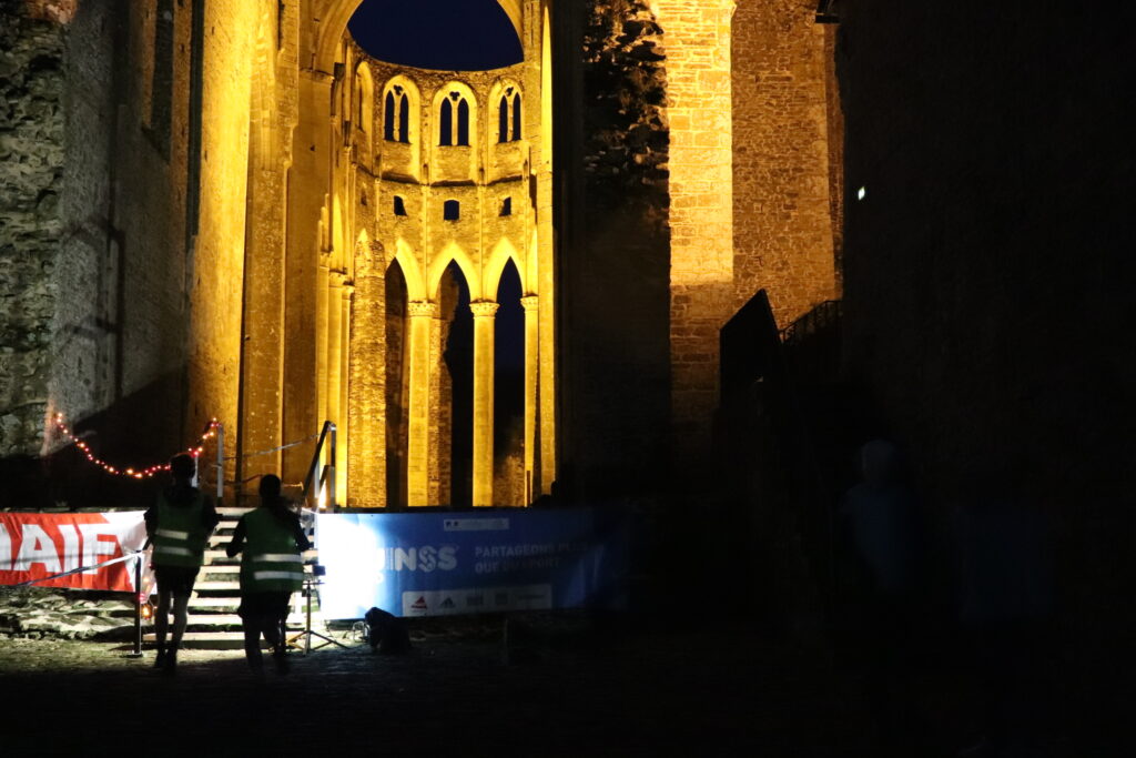Des collégiens en tenue de sport et gilet jaune montant l'escalier de l'église abbatiale. La nuit est tombée et l'église est illuminée.