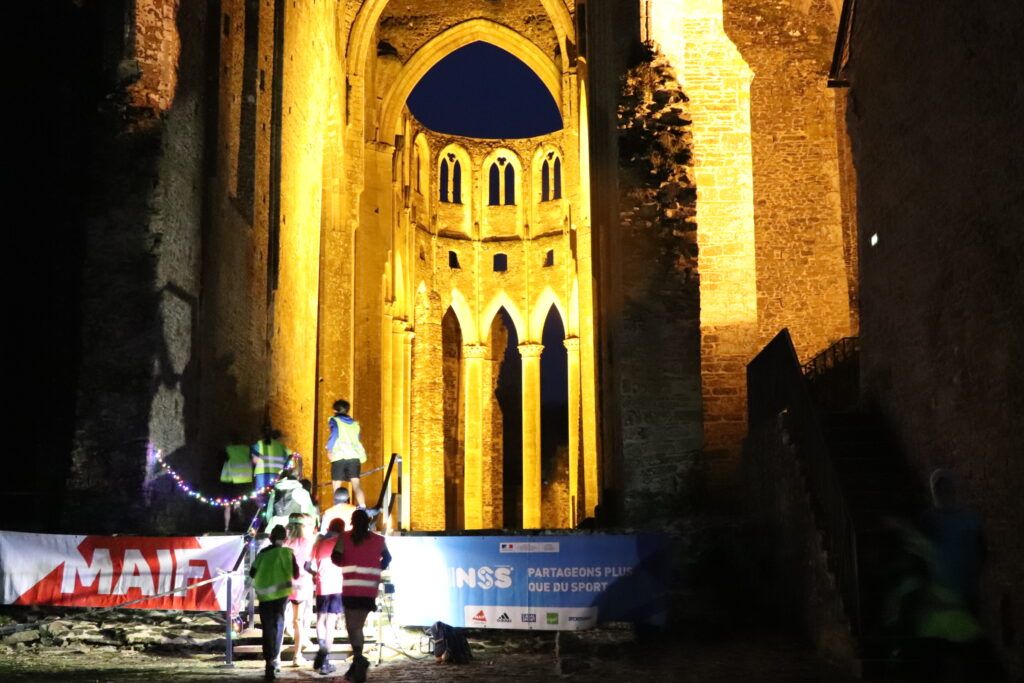 Des collégiens en tenue de sport et gilet jaune montant l'escalier de l'église abbatiale. La nuit est tombée et l'église est illuminée.
