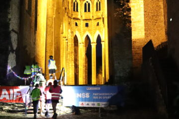 Des collégiens en tenue de sport et gilet jaune montant l'escalier de l'église abbatiale. La nuit est tombée et l'église est illuminée.