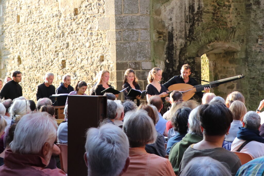 Des chanteurs entrent dans l'église abbatiale dans la lumière du soleil couchant. Des spectateurs les écoutent.