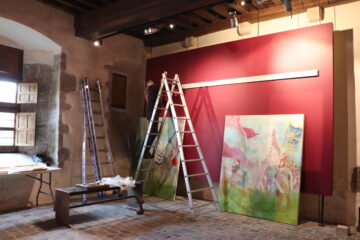 Le technicien des sites et musées du Département accroche le grand diptyque de l'exposition Casus Belli. Les tableaux sont à terre, une échelle est posée devant le panneau peint en rouge.