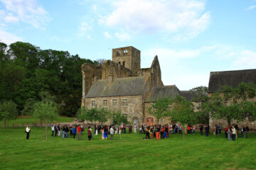De nombreux visiteurs déambulent devant les bâtiments de l'abbaye de Hambye. L'église abbatiale est visible au fond de l'image.