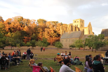 Le soleil couchant éclaire l'église abbatiale pendant que des visiteurs pique-niquent près de la grue.